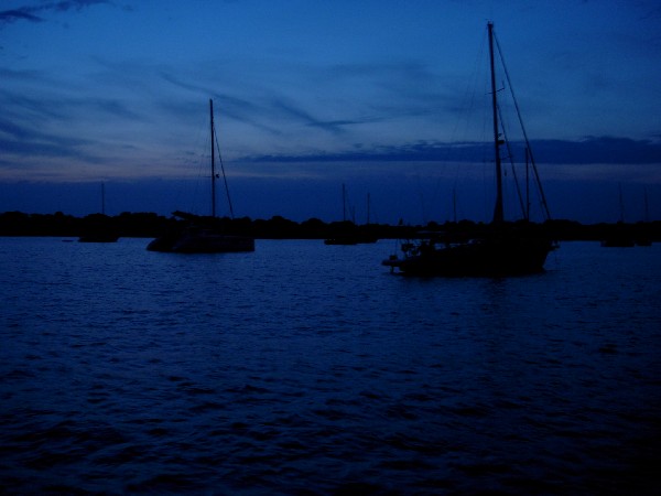 Cae la noche en una tranquila bahia del sur de Menorca. Mientras se prepara la cena, los participantes en el crucero se reunen y charlan en cubierta, bajo las estrellas.